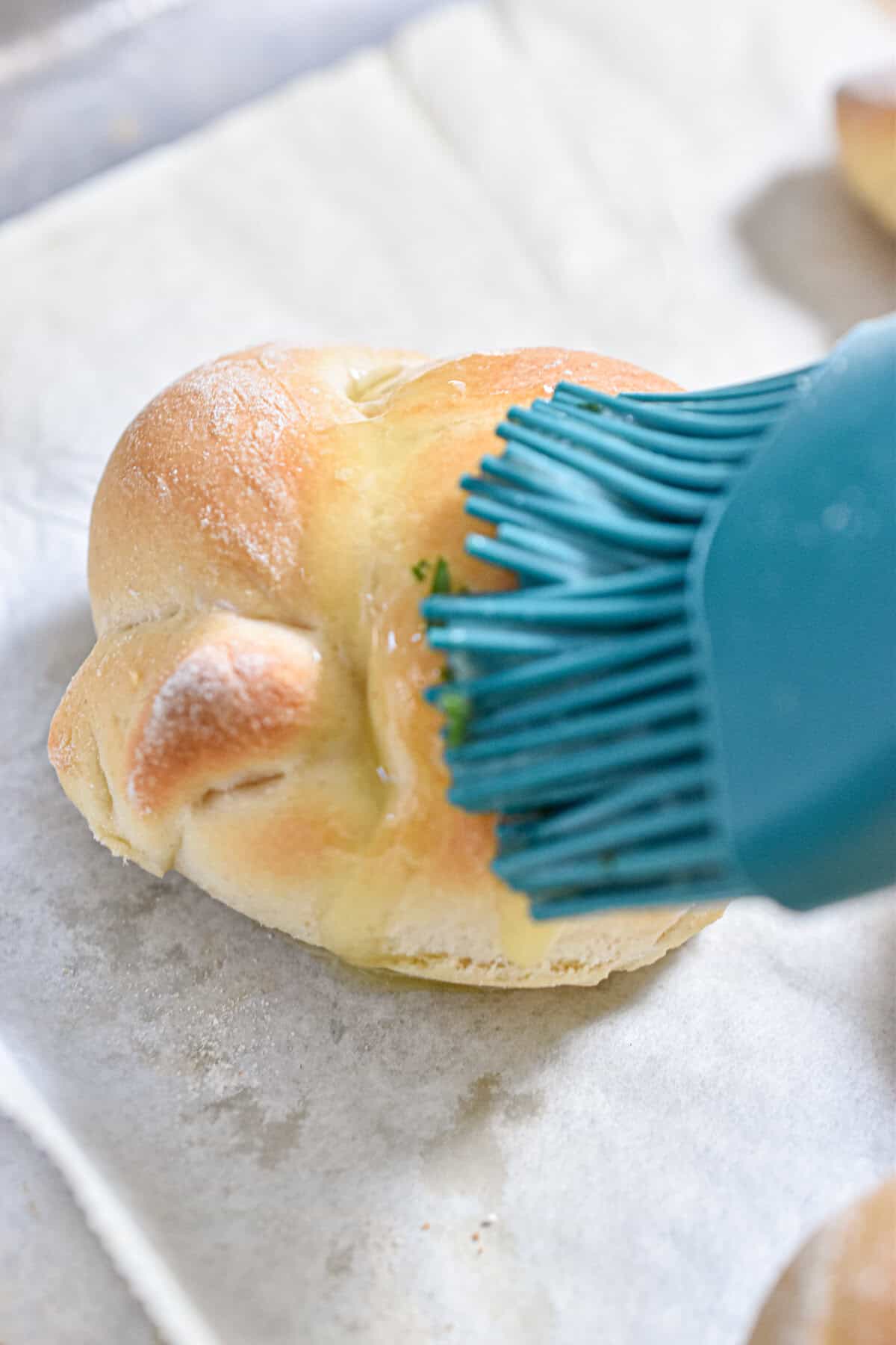A brush is brushing the garlic butter on the sourdough garlic knots.