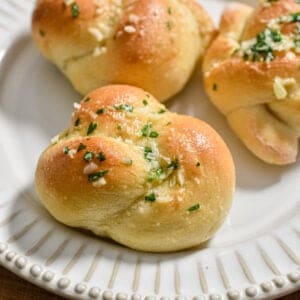 The sourdough discard garlic knot is on a plate topped with parsley and parmesan.