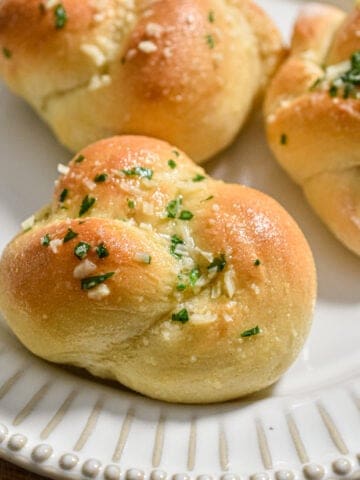 The sourdough discard garlic knot is on a plate topped with parsley and parmesan.